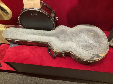 Kırmızı kadife yüzey üzerinde klasik gitar çantası, etiketli sıkıntılı gitar, görülebilir trampet ve akustik gitar parçası, hafif ışıklandırma, kapalı ortam Kyiv, Ukrayna 06-19-2022