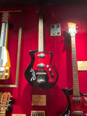 Bir müze sergisindeki kırmızı duvarda eşsiz gitarlar sergilenirken, gitarların altında başka müzik aletleri de görülebiliyor. Bazı elektrikli ve akustik tasarımlar, Kyiv, Ukrayna 06-19-2022