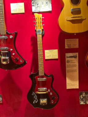 Kırmızı bir arkaplanda sergilenen altı gitardan oluşan bir koleksiyon, her gitarın kendine has özellikleri var. En yakın gitar siyah bir gümrük modeli, onu B Kyiv, Ukrayna 06-19-2022 izliyor.