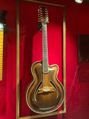 Koyu kahverengi, kırmızı kadife kaplamalı vitrin vitrinli klasik gitar. Cam önü yumuşak ışıklandırmalı ahşap tahıl dokusu T Kyiv, Ukrayna 06-19-2022