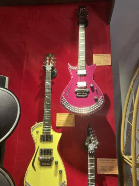Kyiv, Ukrayna 06-19-2022 düzenlenmiş, süslemeleri veya yapay elmasları olan koyu pembe ve sarı elektrikli gitarlara karşı kırmızı bir duvarda dikey gitar görüntüsü