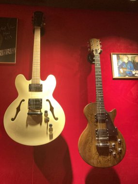 Eşsiz dizayn ve renkten oluşan dört klasik gitar, kırmızı bir duvarda yukarı doğru uzanan dizgilerle daha koyu bir arkaplanda asılı. Gölgeler, Kyiv, Ukrayna 06-19-2022 'nin 3 boyutlu şeklini vurguluyor.