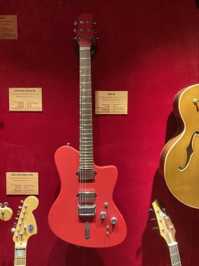 Kırmızı elektro gitar kırmızı bir yüzey üzerinde yatay olarak sergilenmektedir, açık bir şekilde ikinci bir gitar ve arkaplan gitar Kyiv, Ukrayna 06-19-2022 gibi müzik aletleri tarafından korunmaktadır.