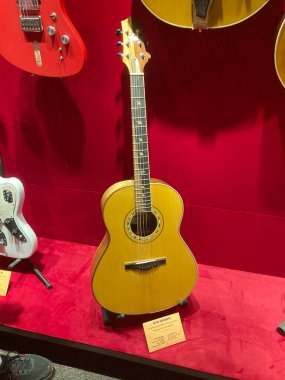Halı döşeli bir zeminde, kırmızı bir zemine karşı bir gitar koleksiyonu. Değişen bitiş vuruşları, güneş patlamaları, doğal ahşap, beyaz, koyu renk. Ön planda klasik bir Kyiv, Ukrayna 06-19-2022 sergileniyor.
