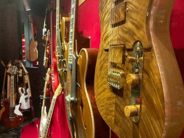 12 gitar, çeşitli tasarım ve renkler, dikey olarak kırmızı bir duvarda sergileniyor, dinamik düzenleme, farklı boyutlarda, yumuşak ışıklandırma, kapsamlı görünüm Kyiv, Ukrayna 06-19-2022