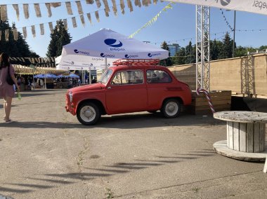Paslı canlı kırmızı bir eski araba, arka planda beyaz çatılı mavi bir çadır da dahil olmak üzere asfalt karton kutuların üzerine park edilmiştir. İndivi Kyiv, Ukrayna 06-19-2022