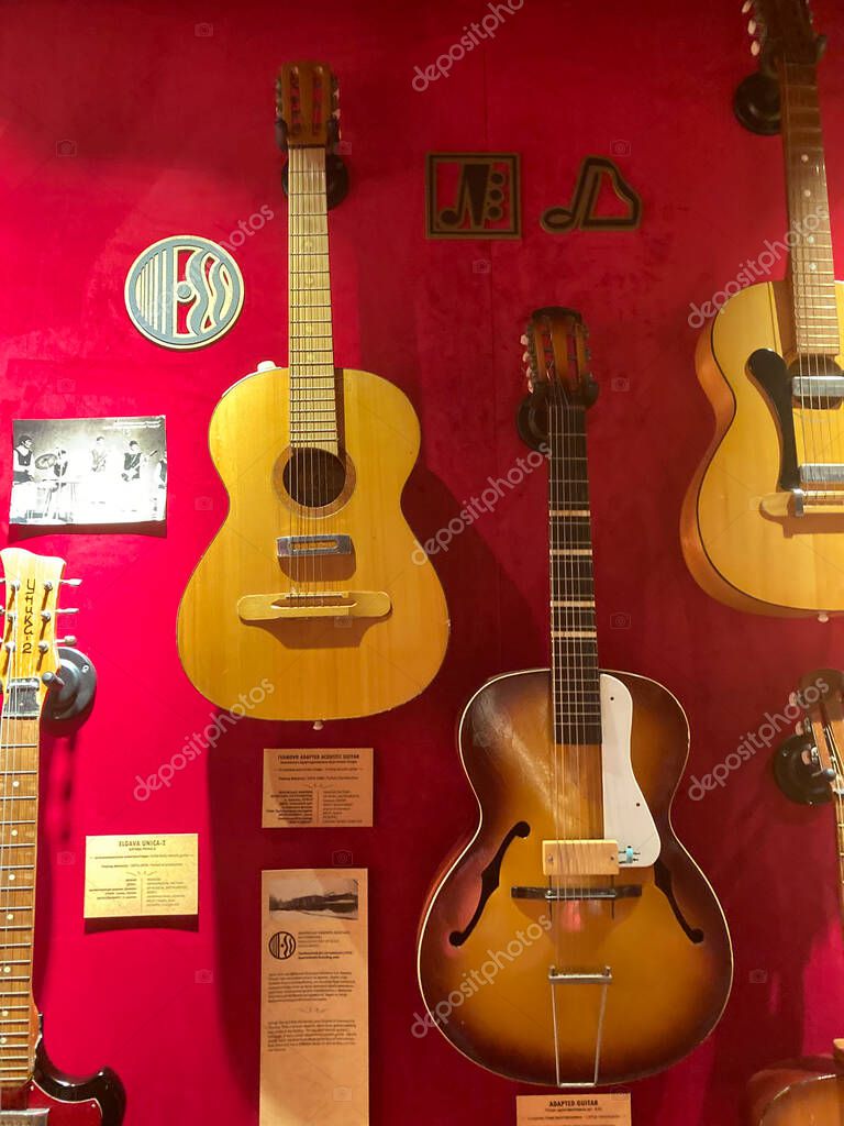 Collection of acoustic guitars displayed against a red backdrop, each with visible strings and pickups Brand label musical noteslogo at top Text providing infor Kyiv, Ukraine 06-19-2022