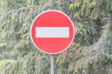 Kırsal ya da doğal bir ortamda iki metal direğe monte edilmiş, yumuşak ve dağınık ışık altında yemyeşil yapraklarla çevrili köşegen bir dur işareti.