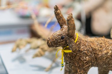 Kurumuş palmiye yapraklı hayvan heykelinin yakın çekimi, sarı kumaşla süslenmiş, üst ışık kaynağı dokusu ve işçiliği ön plana çıkarıyor.