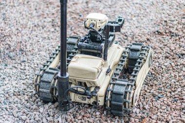 Düz zeminde gri ve siyah, altı bacaklı robotik bir araç, muhtemelen mayınların temizlenmesi için kullanılıyor, kontrol panelleri, ekranları ve kabloları var.