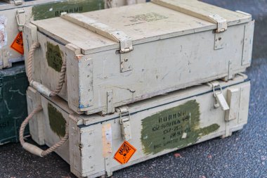 Açık hava cephane sandıkları, muhtemelen ahşap ya da metal, görünür işaretler ve aşınmış kenarlar yayılmış ışıklandırma altında asfalt bir yüzeye yerleştirilmiş.
