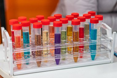 Renkli cam test tüplerinin toplanması şeffaf bir plastik tutacağa yerleştirilmiş, mavi, yeşil, sarı, mor renkte çeşitli sıvılar içeriden görünür, yapay zeka ile aydınlatılır.