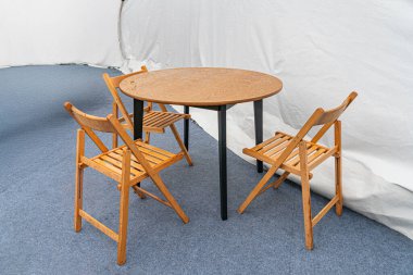 Yuvarlak ahşap masa, dört katlanır sandalye hafif ahşap çerçeve, dokunmuş koltuk, mavi halı döşeme gerçekçi stil, hatta yapay kaynaktan ışıklandırma, insan veya metin bile yok.