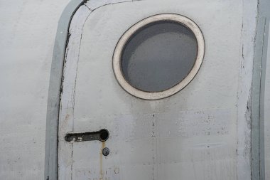 Eski bir uçak tarafının yakın görüntüsü, kapı kolu ve mandalları olan bir pencere, dağınık ışık, ince aşınma ve gölgeler.