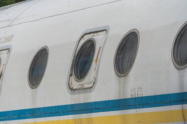 Yansıtıcı, eşit aralıklı, yuvarlak pencereli ve gündüz aydınlatmasının altında sarı şeritli beyaz bir yolcu uçağına yakın çekim.