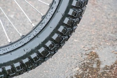 Posta elektrikli bisiklet tekerleğinin yakın çekimi, bulanık arka planda su damlacıkları olan siyah off-road lastiğine odaklan.