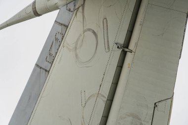 Gümüşi metalik bir kanadın yakın görüntüsü, görünür çizikler ve izler, muhtemelen motor ya da ekipman panelleri ile, aşağıdan yukarıya bakan sisli bir gökyüzü arka planına karşı.