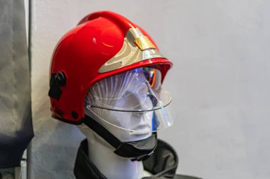 Beyaz ve altın aksanlı kırmızı bir itfaiyeci kaskı takan başsız bir manken desenli duvar kaplamasına dayanır. Kaskın siyah bir çene kayışı var.