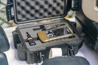 Üzerinde birden fazla lens ve koruyucu kapaklı siyah bir cihaz bulunan engebeli bir kutu, muhtemelen bir akıllı telefon veya kamera, onun yanında bir lens kapağı ve potansiyel bir ek lens veya filtre bulunur.