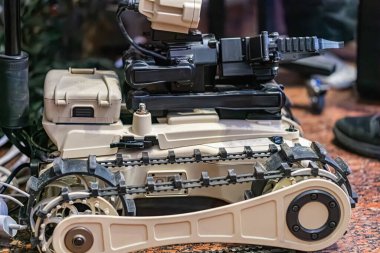Kapalı alanda kullanılan bej bir robotik tankın yakın plan görüntüsü. Tankın üstünde kamera, sensör sistemi ve diğer elektronik ekipmanlar var.