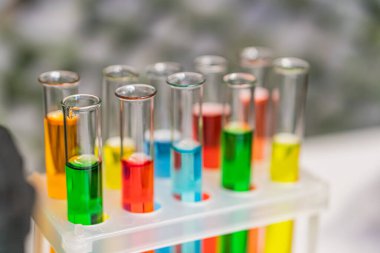Test tüplerinin çeşitli renkli sıvılarla dolu bir tepside dizilmesi, sırayla mühürlenmiş ve hizalanmış, muhtemelen bir laboratuvar ortamında, parlak ışık altında.