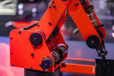 Büyük, canlı, kırmızı bir robotik kol ve birden fazla eklem ve segmentlere sahip kapalı bir ortam. Gri yansıtıcı zemini var. Hiçbir insan ya da diğer nesne ayırt edici değil.