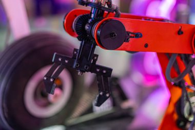 Hafif ışıklandırılmış endüstriyel ortamda mobil üsteki kırmızı metalik robot kolunun yan görüntüsü.