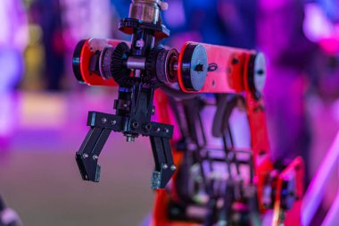 Kırmızı ve siyah robotik bir kolun yakın plan görüntüsü, birden fazla eklemli, morumsu bir zemin üzerinde sergileniyor..