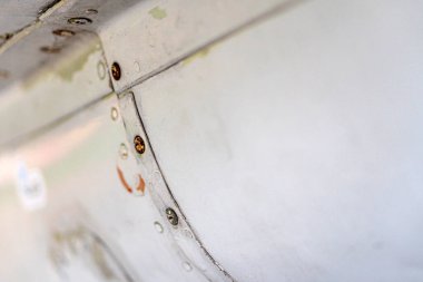 Yıpranmış bir uçağın kanat ucunun yakın çekimi, ağırlıklı olarak beyaz çizikler, boya kırıntıları, perçinler ve yatay bir çizgi, gerçekçi stil, yüksek kontrastlı, doğal ışık altında kimse karşı karşıya değil.