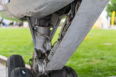 Geniş iniş takımları ve yıpranmış metal parçaları olan bir jet yolcu uçağının göbek altı görüntüsü muhtemelen bir havaalanı ya da havaalanı yakınında, doğal ışık altında.