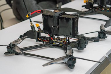 Bir yüzeyde parçalanmış savaş kuadkopter dronu, kablolama ve devre kartı gibi görünür iç bileşenleriyle karanlık vücut sarı konnektörlerle ya da kapalı mekandaki düğmelerle çelişir, nötr ışık ayarlarıyla.