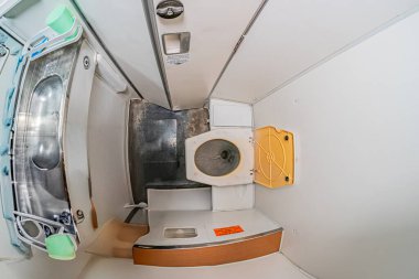 Lavabosu, atık kutusu ve kontrol paneli benzeri nesnesi olan küçük bir uçak gemisi tuvaleti. Renk şeması, sessiz gri, beyaz, görünür metin ya da insanlar yok.