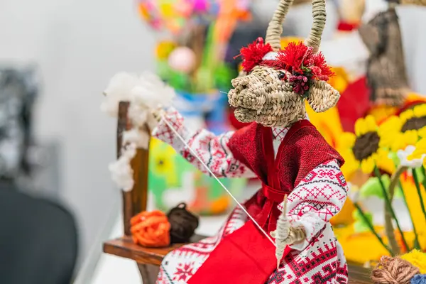 Turuncu minderli sandalyede oturan canlı bir Ukraynalı halk figürünün yakın plan resmi kağıt ve kumaştan yapılmış olan figür kırmızı, beyaz ve yeşil desenli geleneksel kıyafetler giyiyor.