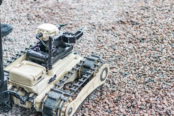 Görüntü bej bir insansı robotik deminer tasvir ediyor, kayalık arazi modüler yapısında kısmen görülebilir, gölgelenmiş varyasyonlarla sol üstten doğal aydınlatma.