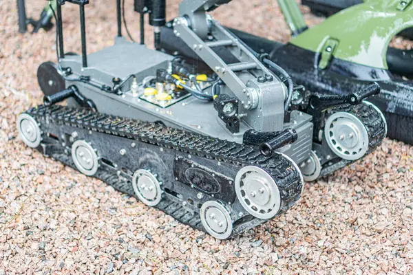 Robotik mayın temizleme cihazı, çoklu eklemli kollar, kayalık arazi veya simülasyon düzeni, metalik renk şeması, hatta ışıklandırma, teknik fotoğraf tarzı