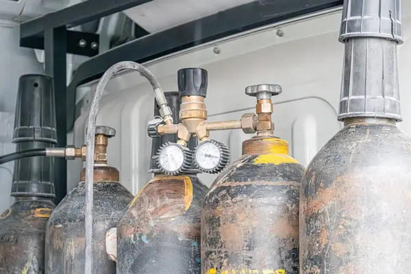 Endüstriyel ortamda birbirine bağlı aşınmış silindirik oksijen tankları. Yumuşak gölgeler, gizli fotoğraf stili, metin ya da insan figürü yok. Belgesel stili C 'yi göstermeyi amaçlıyor.