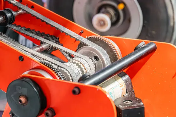 Şeffaf bir kapak altında karmaşık bir dişli ağı ve kemer ağı içeren kırmızı endüstriyel bir robot kolunun yakın planı, kapağa küçük, okunabilir bir kağıt iliştirilerek bulanıklaştırılmıştır.