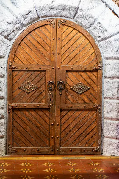 Yıpranmış taş kemer yolu oyulmuş ahşap kapılar birbirine kenetlenmiş deseni gösteriyor, tarihi mimaride ayarlanmış yukarıdan gelen aydınlatma sakin ama heybetli bir atmosfer yaratıyor.