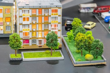 Üç katlı apartmanlı minyatür şehir yerleşim modeli, açık kahverengi ve beyaz renklerin karışımı, korkuluklu balkonlar, uydu antenleri, zemin katlı girişler, yeşil alan, küçük ağaçlar
