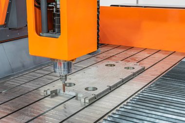 Başta turuncu ve metalik olmak üzere endüstriyel çelik makinelerin, loş ışıklandırılmış bir fabrikada, kaldıraç, dişli ve muhtemelen hidrolik gibi mekanik bileşenler kurarak, tepe noktasından vurulması.