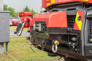 Bulutlu gökyüzünün altındaki çimenli alanda kurtarma ekipmanlarıyla kırmızı itfaiye aracı, su hortumları, arka planda ağaçlar.