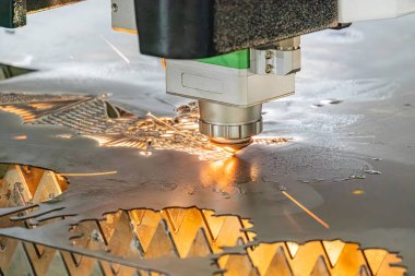 Büyük endüstriyel lazer devrede. Karmaşık metal parçaları sondajlanıyor. Odaklanmış parlaklık üretim sürecinin hassasiyetini vurguluyor.