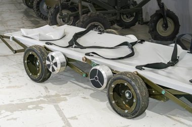 İçinde askeri bir çöp, ATV ve zeytin yeşili bir tuvalin üzerinde uzun ömürlü sedye, doğal ışıklandırma, görülebilir insan yok.