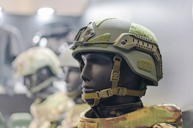 Koruyucu gözlük ve ilave ekipman kayışları takan kasklı bir figüre odaklanarak üç asker miğferi gösteren birleşik bir resmin ayrıntıları o kadar bulanık ki