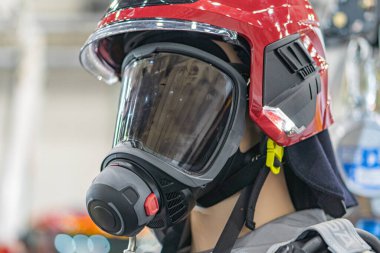 Daha çok siyah aksanlı, koyu renk alevlere dayanıklı bir üniforma giyen ve bağlı bir güneşlik takan itfaiyeci kaskının yakın çekimi.