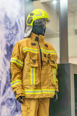 Sarı yansıtıcı giysili itfaiyeci, ayakta duruyor, arka planda gölgeler var..