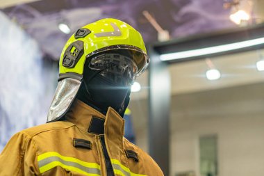 Yansıtıcı çizgili sarı koruyucu elbiseli itfaiyeci, başlık ve aksesuarlarla donatılmış bir siluet grafiğine karşı duruyor. Görünürde hiçbir metin yok. Resim tarzı basit.