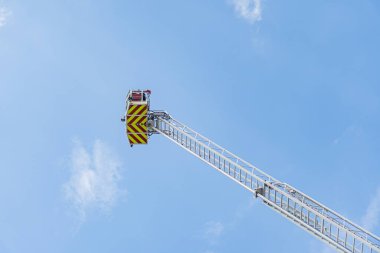 İtfaiye merdiveni uzantısı, merdivendeki itfaiyeci, açık mavi gökyüzü, beyaz kamyon, siyah ve sarı çizgili merdiven, koyu renk elbise, parlak güneş ışığı