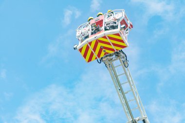 Kırmızı ve sarı çizgili merdivenin yakın görüntüsü itfaiye aracından yayılan açık mavi gökyüzüne doğru dağınık bulutlarla çevrili.