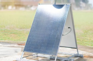 Çimenli bir alanda güneş paneli dizisi, bulutlu bir gökyüzünün altında iki sıra açılı panel biri yukarı eğimli, diğeri düz, parlak hücreler ışık kontrol kutusu veya bağlantı kutusu yansıtan